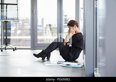 Sovraccaricato imprenditrice seduta sul pavimento in office Foto Stock