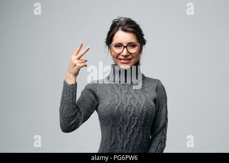 Ragazza gioiosa in bicchieri dimostrando segno di vittoria Foto Stock