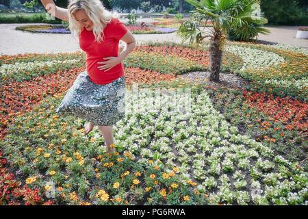 Felice donna incinta a piedi attraverso fiori che sbocciano in posizione di parcheggio Foto Stock
