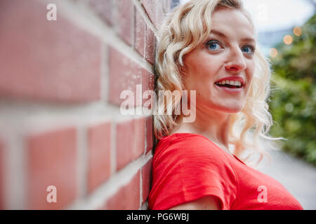 Ritratto di donna bionda all'aperto appoggiata contro un muro di mattoni Foto Stock