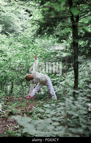 Senior donna fare yoga nella foresta, triangolo pongono Foto Stock