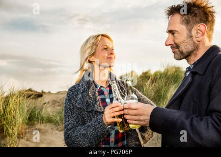 Coppia sorridente in dune tintinnio di bottiglie di birra Foto Stock