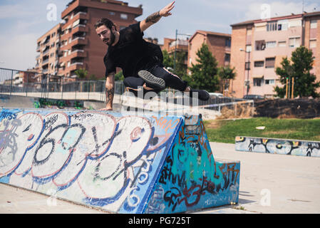 Tatuato uomo che fa parkour in uno skatepark Foto Stock