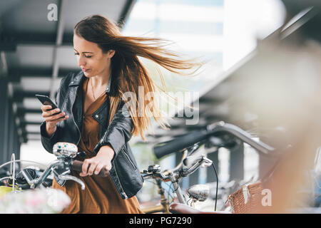 Giovane donna con la bicicletta utilizzando il cellulare in città Foto Stock