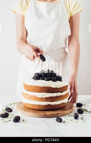 Ritagliato colpo di donna decorare appena sfornato torta blackberry sul piedistallo di vetro su bianco Foto Stock