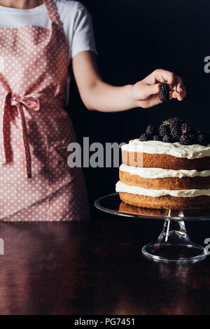 Ritagliato colpo di donna decorare appena sfornato torta blackberry sul piedistallo di vetro su nero Foto Stock