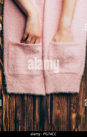 Immagine ritagliata donna mettendo le mani nelle tasche del maglione rosa sul tavolo di legno Foto Stock