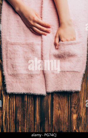 Immagine ritagliata donna mettendo le mani nelle tasche del maglione rosa sul tavolo in legno Foto Stock