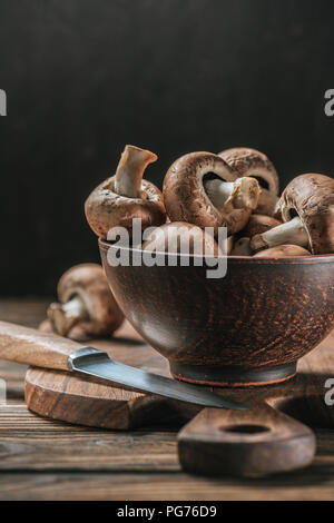 Mature funghi cremini nella ciotola sul tavolo di legno isolato su nero Foto Stock