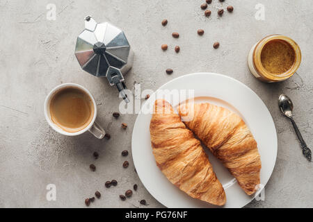 Vista superiore della tazza di delizioso caffè con croissant e moka pot su una superficie in calcestruzzo con schizzi di caffè in grani Foto Stock