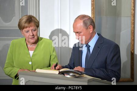 Il presidente russo Vladimir Putin firma il libro degli ospiti come il Cancelliere tedesco Angela Merkel guarda al chancellors Meseberg residence Agosto 18, 2018 al di fuori di Berlino, Germania. Foto Stock
