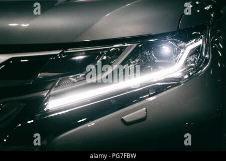 Faro di auto e il cofano di potenti sport auto blu con riflessi blu su sfondo scuro. Chiudere fino al faro di auto. Foto Stock