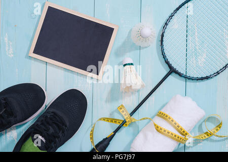 Vista dall'alto di attrezzature sportive, orologio, nastro di misurazione, scarpe, acqua in bottiglia, asciugamano, badminton racchetta e volano, uno stile di vita sano e concetto di fitness Foto Stock