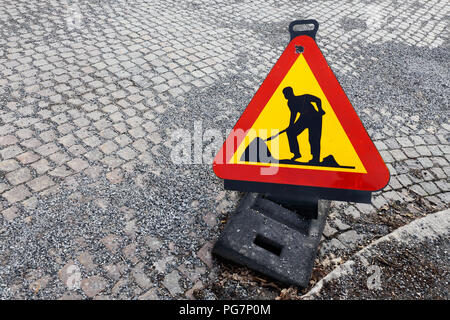 Angelo alta vista di un triangolo a forma di lavori temporanei cartello segnaletico posto su una strada pavimentata con cobbelstones con ghiaia sulla parte superiore. Foto Stock