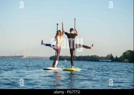 Stand Up Paddle board yoga eseguita da una bella giovane sullo sfondo luminoso, formazione yoga sulla spiaggia Foto Stock