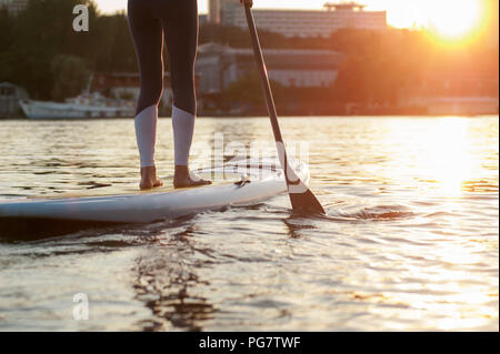 SUP fiducioso del costume da bagno donna in piedi con un dispositivo di compressione sulla tavola da surf, gambe Foto Stock