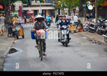 Una donna che indossa conica tradizionale cappello di paglia cavalca una bicicletta nell'UNESCO protetti città di Hoi An, Vietnam centrale. Foto Stock