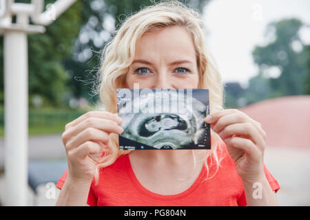 Ritratto di felice donna incinta azienda immagine ad ultrasuoni all'aperto Foto Stock