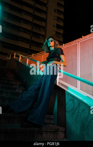 Elegante giovane donna di notte nella città, indossando occhiali da sole Foto Stock