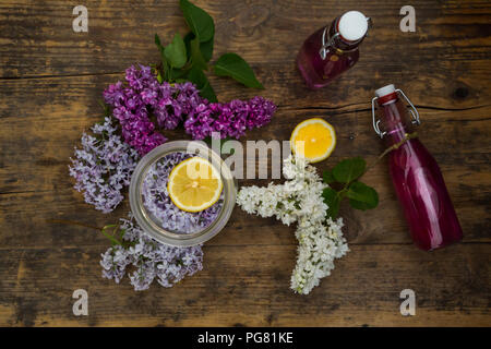 Due bottiglie di vetro di casalinghe sirup lilla e ingredienti su legno Foto Stock