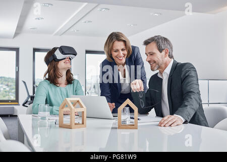 La gente di affari avente una riunione in ufficio con occhiali VR, laptop e modelli architettonici Foto Stock