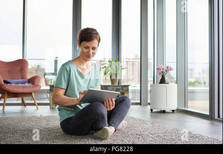 Donna seduta sul pavimento di casa utilizzando tablet Foto Stock