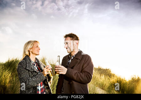 Coppia sorridente in dune tintinnio di bottiglie di birra Foto Stock