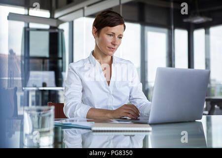 Imprenditrice seduti al tavolo di vetro in ufficio utilizzando laptop Foto Stock