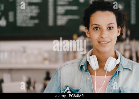 Giovane donna con le cuffie, lavorando in coworking space Foto Stock