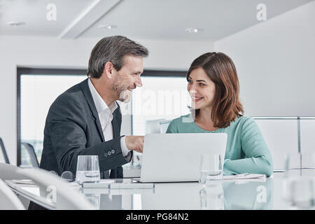 Imprenditore e imprenditrice avente una riunione in ufficio con computer portatile Foto Stock