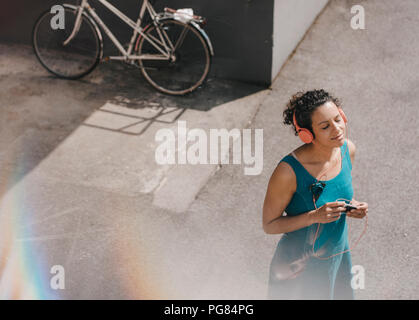 Donna in piedi nel cortile, indossa le cuffie e ascoltare della musica Foto Stock