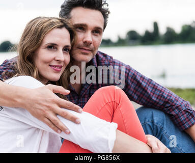 Affettuosa felice coppia seduta al Riverside Foto Stock