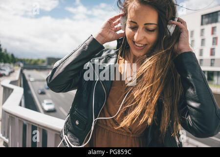 Sorridente giovane donna ascolto di musica sul ponte autostradale Foto Stock