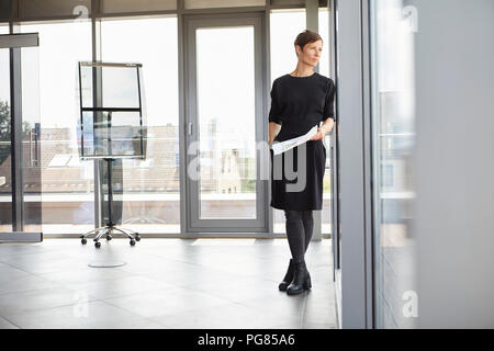 Imprenditrice in piedi in ufficio guardando fuori della finestra Foto Stock