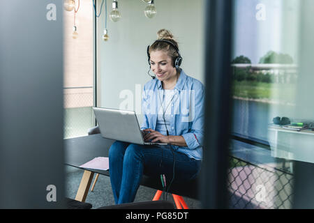 Giovane imprenditrice seduto alla scrivania, esecuzione di una chiamata utilizzando la cuffia e il computer portatile Foto Stock