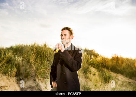 Donna sorridente di bere una birra in Dune Foto Stock