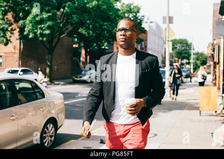 Stati Uniti d'America, New York, Brooklyn, uomo a camminare per la strada, tenendo tazza di caffè Foto Stock