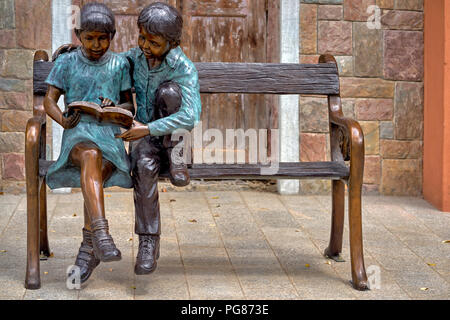 Statua ragazzo e ragazza seduta su una panchina, lettura libro, insieme. Insieme Foto Stock