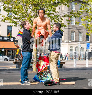 Edinburgh Fringe Festival di Edimburgo, Scozia, Regno Unito. 24 agosto 2018. Il sole splende sui frequentatori della frangia in Bristo Square. Un giapponese street performer di Bristo Square con membri del pubblico di partecipanti in un acrobatico stunt Foto Stock