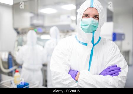 Tecnico di laboratorio che indossa una tuta protettiva e maschera per il viso in un laboratorio che deve mantenere un ambiente sterile. Foto Stock