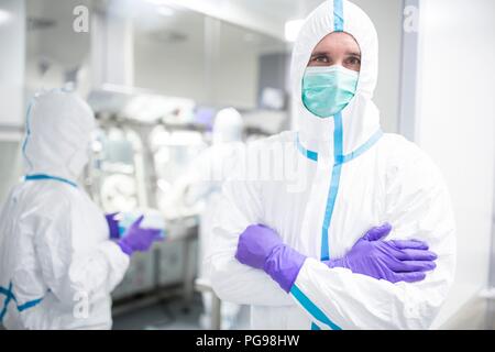 Tecnico di laboratorio che indossa una tuta protettiva e maschera per il viso in un laboratorio che deve mantenere un ambiente sterile. Foto Stock