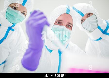 Tecnici di laboratorio indossando tute protettive e maschere facciali in un laboratorio che deve mantenere un ambiente sterile. Foto Stock