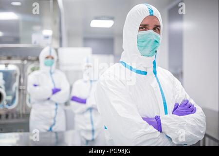 Tecnici di laboratorio indossando tute protettive e maschere facciali in un laboratorio che deve mantenere un ambiente sterile. Foto Stock