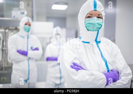 Tecnici di laboratorio indossando tute protettive e maschere facciali in un laboratorio che deve mantenere un ambiente sterile. Foto Stock