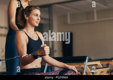 Donna seduta su una formazione pilates macchina tirando fascia elastica con la sua mano. Foto Stock