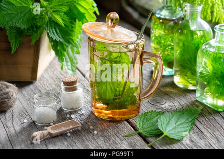 Salutare tè di ortica, bottiglie di infusione, Ortica piante e bottiglia di globuli omeopatici su un tavolo di legno. L'omeopatia e la medicina di erbe. Foto Stock