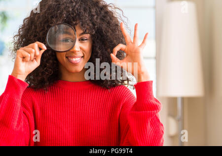 Curioso americano africano donna guardando attraverso la lente di ingrandimento facendo segno ok con le dita, simbolo eccellente