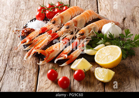 Preparazione per la cottura di materie langoustine, gli scampi con verdure, erbe aromatiche e spezie close-up su una scheda su una tavola di legno orizzontale. Foto Stock