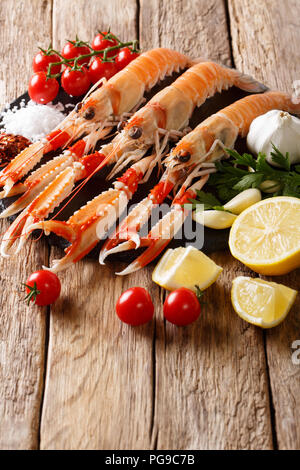 Crudo fresco langoustine, gli scampi con verdure di stagione e le erbe closeup su una piastra su un tavolo di legno. verticale, rustico Foto Stock