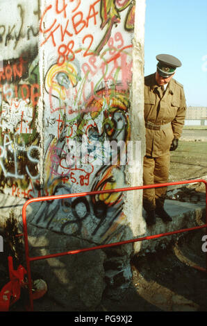 Un Oriente poliziotto tedesco guarda ad un piccolo albero di Natale che ornano il tedesco-occidentale della parte del muro di Berlino. La protezione è in piedi al creato di recente apertura nel muro di Berlino a Potsdamer Platz. Foto Stock